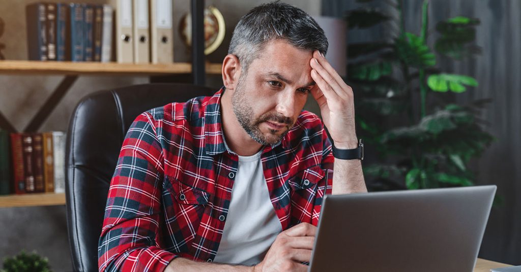 middle aged man having stressful time working on laptop from home office