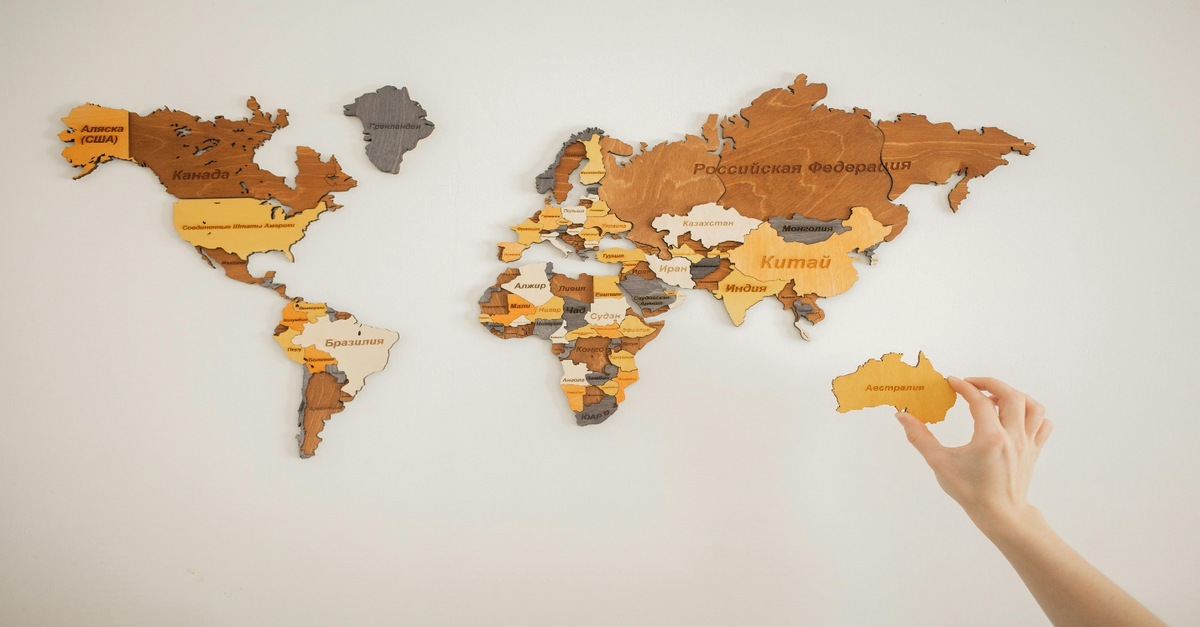 Wooden continents pieced together on a white surface with a hand holding Australia, symbolizing global business expansion and highlighting how Sage Consultants can assist with systems like Sage 300 or Sage Intacct.