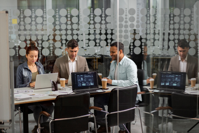 A team of people sit together at a desk with laptops and notebooks to provide streamlined IT solutions as outlined in this Managed IT Services guide