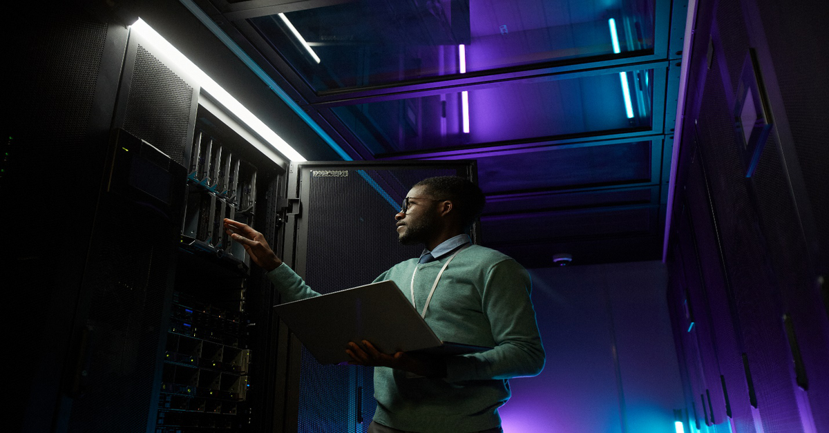 A man holding a laptop works on a server tower, ensuring network security, as outlined in this Managed IT Services guide