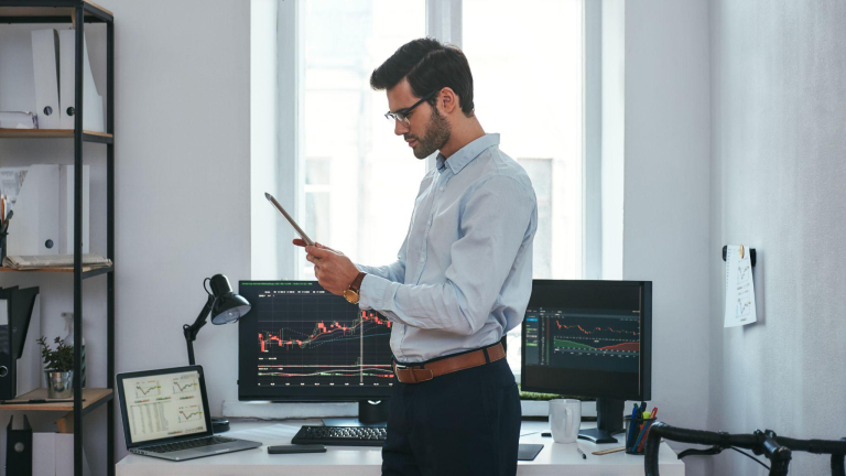 Business professional reviewing financial data on tablet with performance charts displayed behind him, representing scalability in ERP and custom financial systems