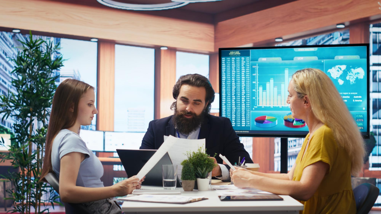Finance professionals analysing reports in front of a large analytics dashboard, symbolising integrated ERP reporting and operational visibility.
