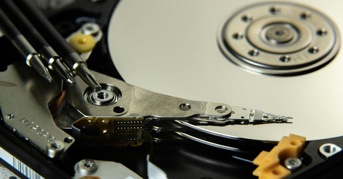 Close-up of a silver and black hard disk with various components and three screwdrivers of different sizes, representing the diverse range of data backup solutions available to businesses through a Managed IT Services Provider.