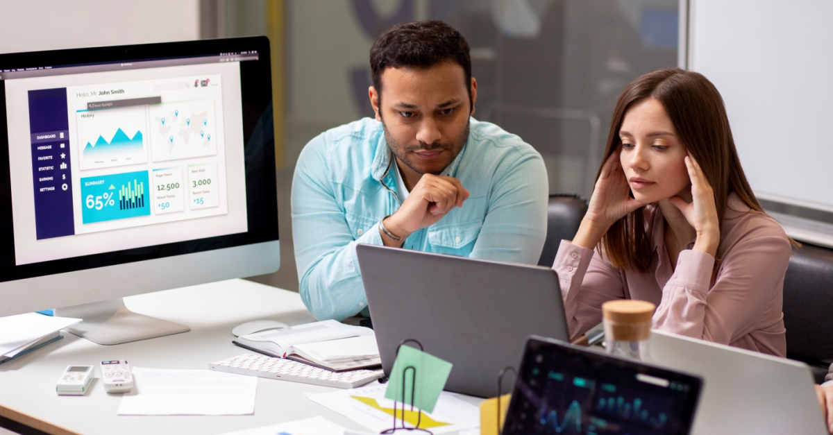 A man and woman sitting inside an office, looking at their computer screens, deciding the right managed IT service provider