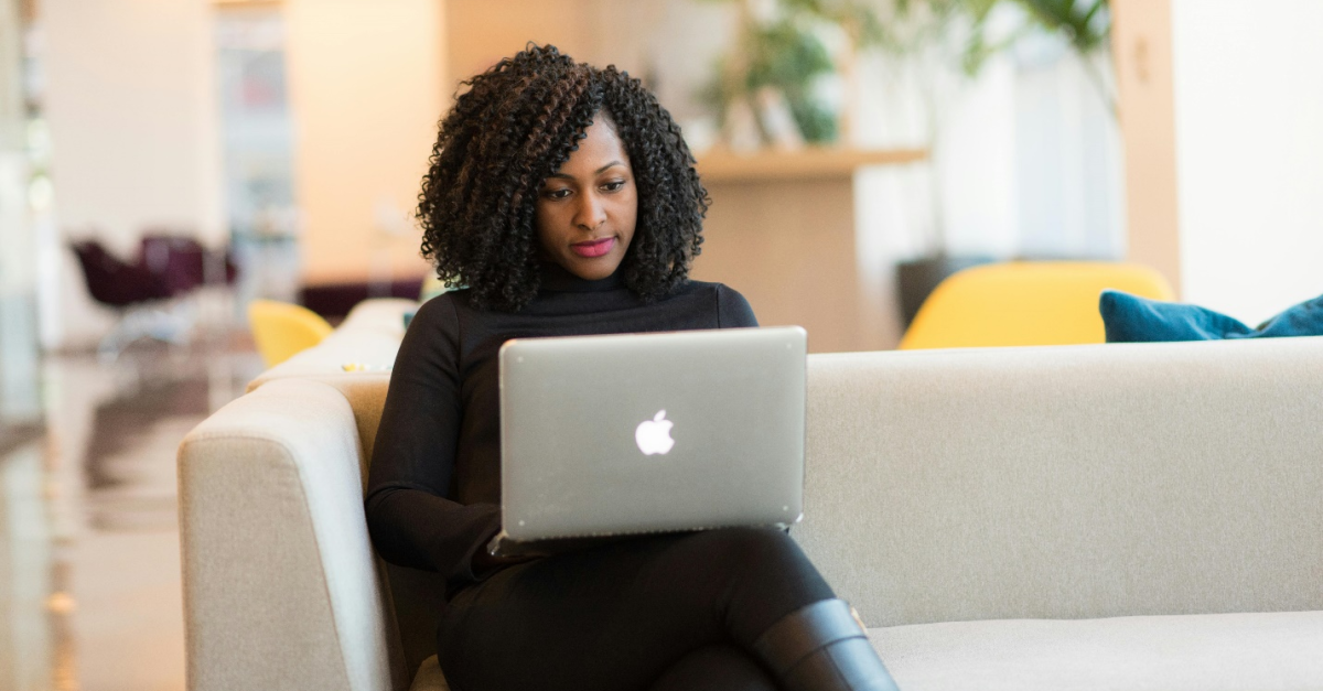 Image of a woman sitting on a beige sofa with a MacBook, an office, and a plant in the background, indicating Sage Consultants' assistance in migrating to Sage Intacct.