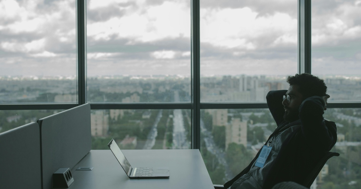 Person sitting at a desk with hands behind head, looking frustrated in front of a laptop, overlooking a cityscape beneath a cloudy sky, highlighting the frustration caused by data loss and the need for data backup solutions provided by a Managed IT Services Provider.