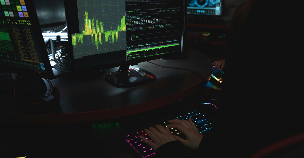 A person’s hands on a keyboard with blue and pink backlights in front of a screen showing data and code, highlighting the importance of Cyber Security Services and Network Infrastructure Security.